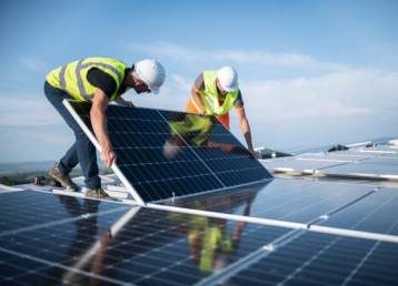 Team of two engineers installing solar panels on roof.